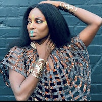 a black woman in a colorful outfit posing against a brick wall